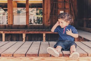 little boy sat on decking outside