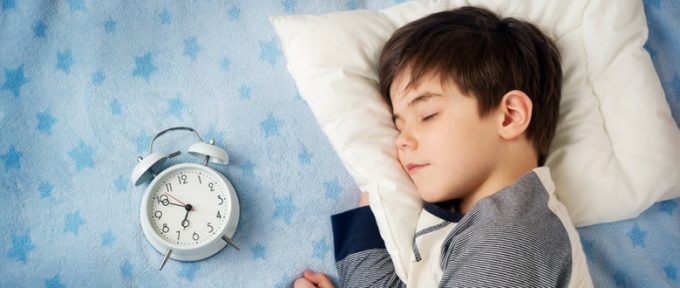 little boy in bed with a clock beside him