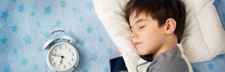 little boy in bed with a clock beside him