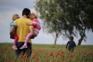 man holding 2 children and 1 running in the field
