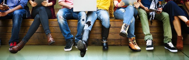 young people sat on a bench reading from laptops