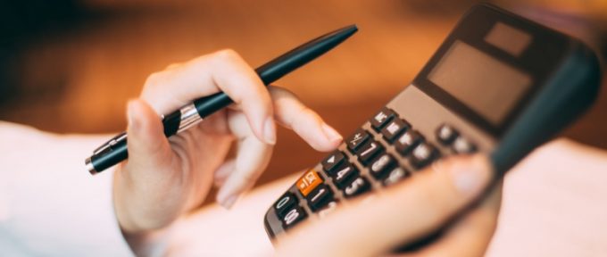 pen in hand holding onto a calculator