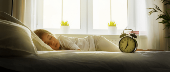 child asleep in bed next to alarm clock