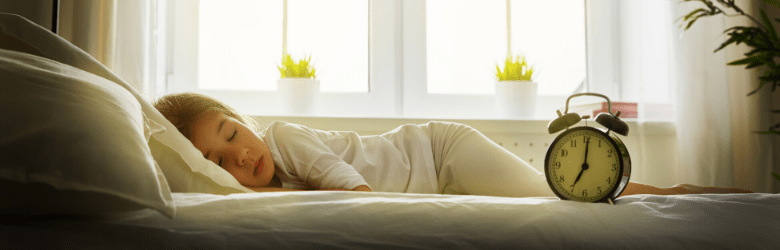 child asleep in bed next to alarm clock