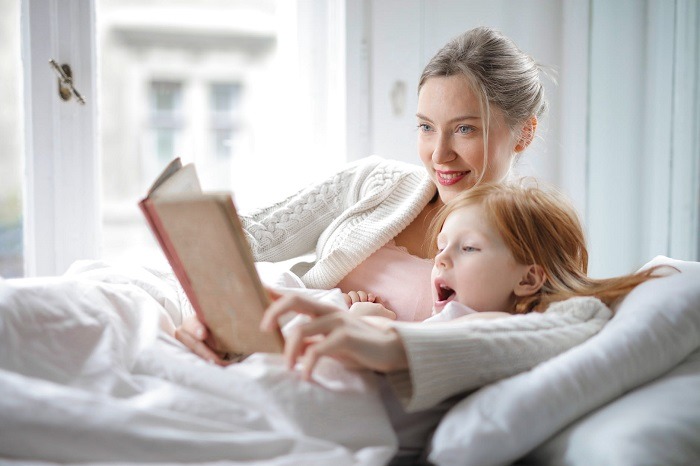 mother and daughter reading book in bed