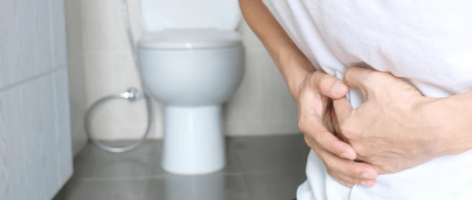 man constipated holding stomach near the toilet