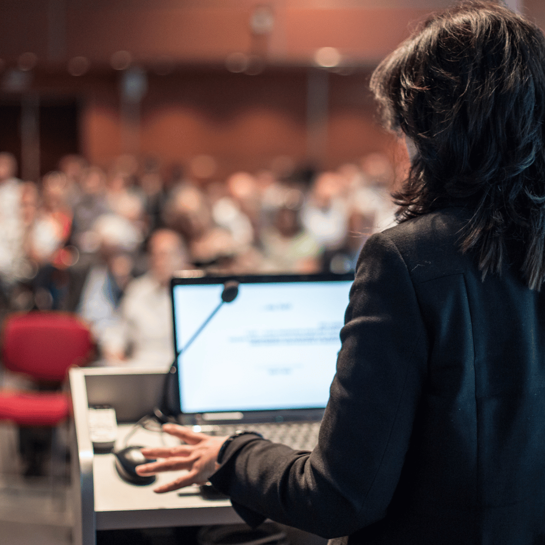 An image of a seminar speaker from behind talking to the crowd