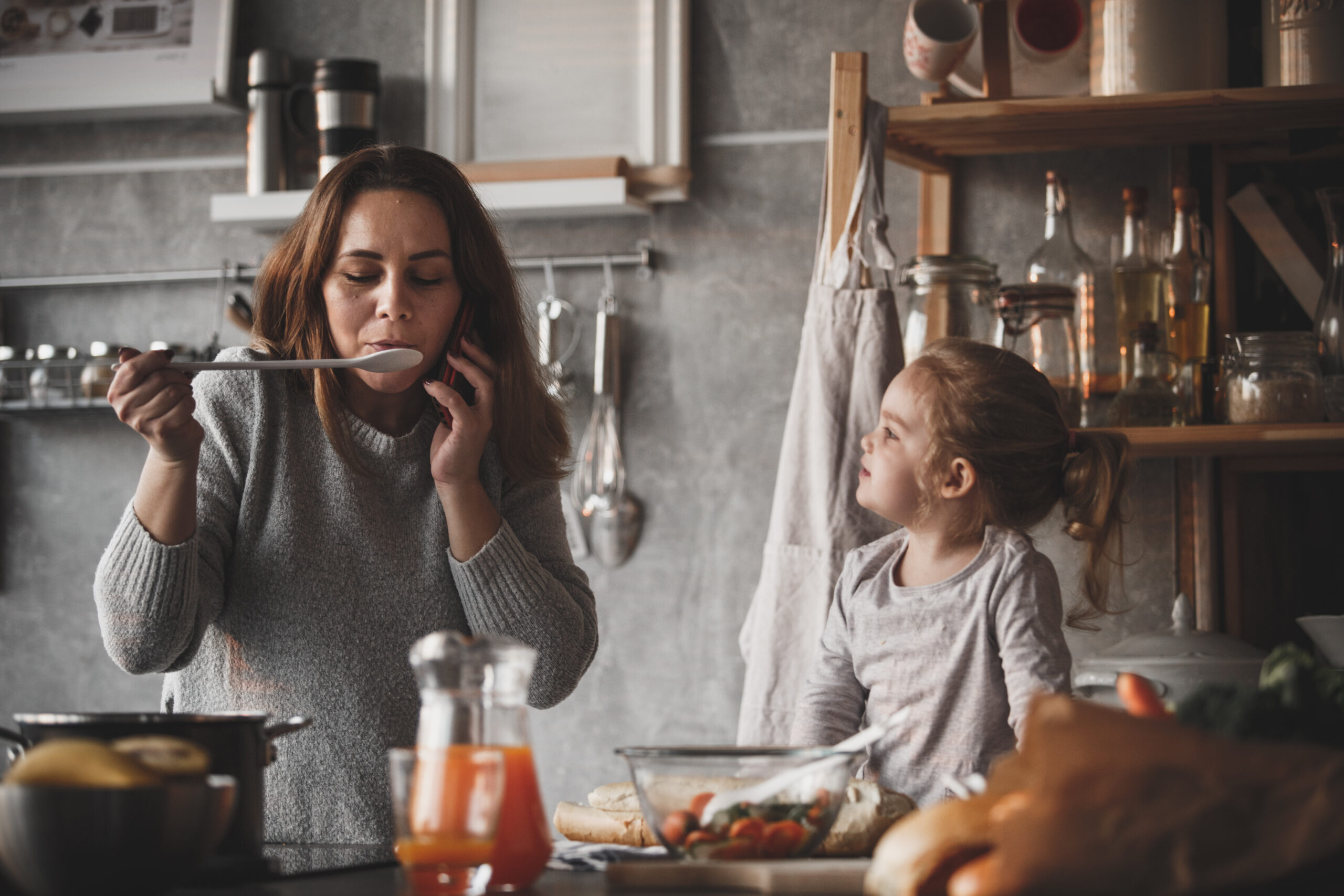Mother and daughter cooking together, woman talking on the phone.