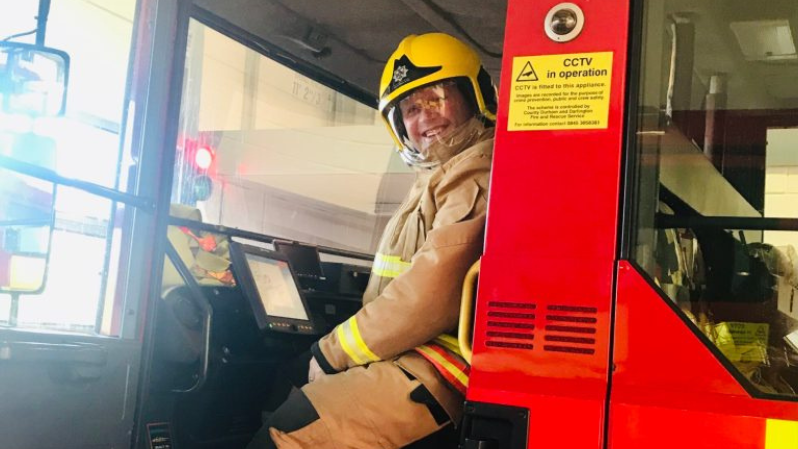 A fireman is sat in the seat of a fire engine