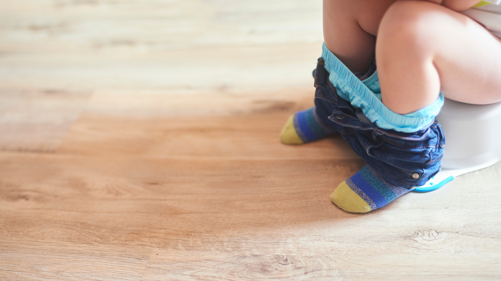 a child sat on a potty - only their legs and knees are visible