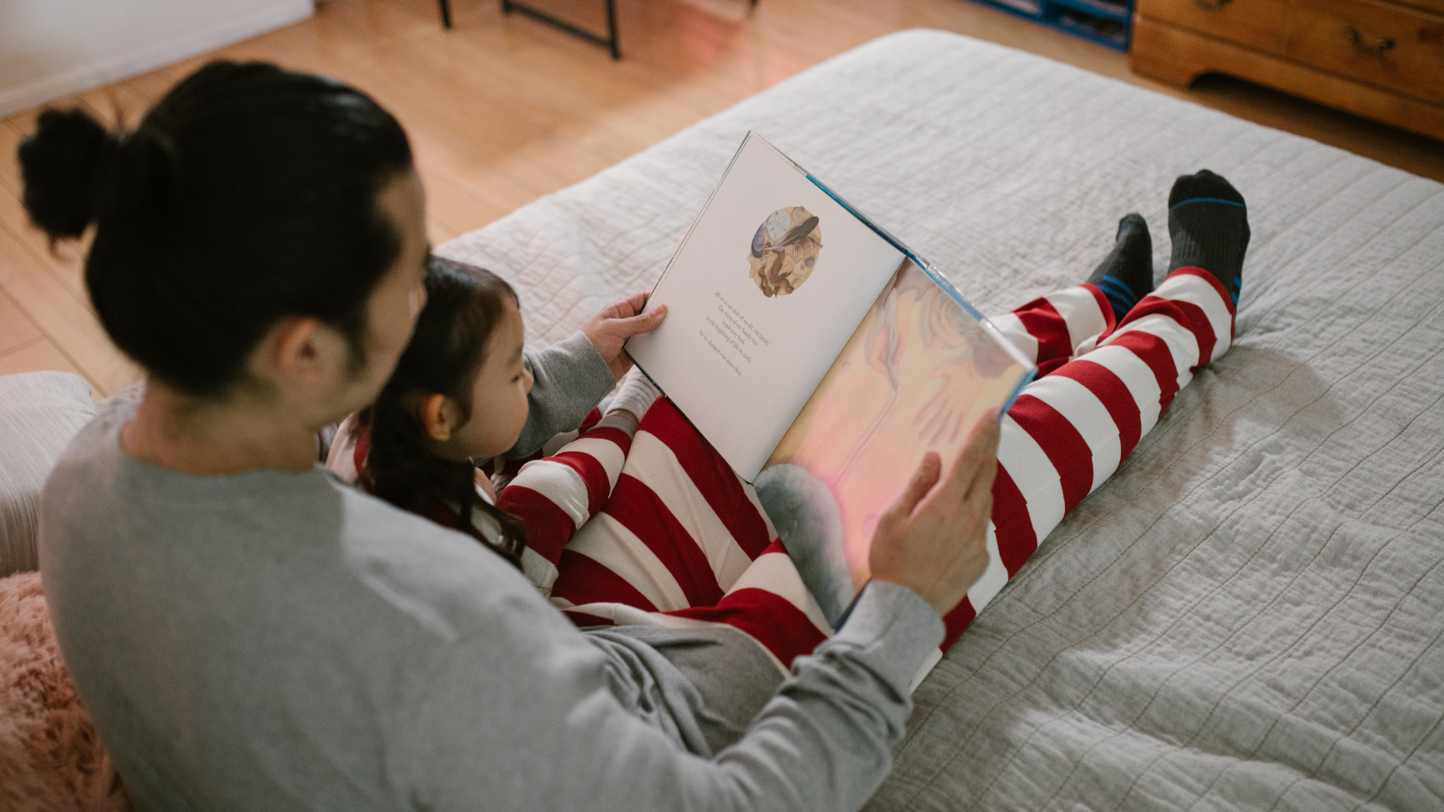 a dad and daughter sat on the floor reading a book in pyjamas
