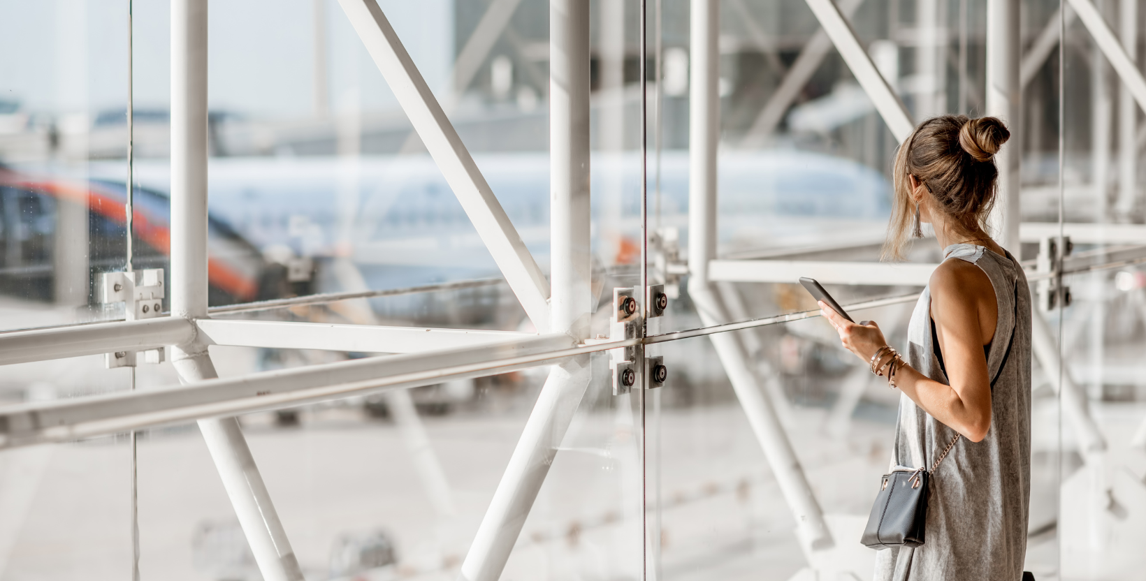 A stock image of an airport with a lady who is travelling looking out the window at the planes. The image represents travelling with a continence problem.
