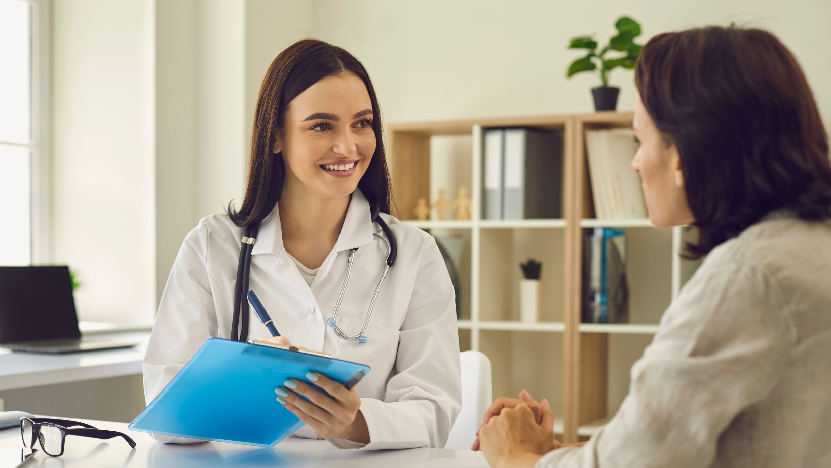 A female medical professional holds a clip board and smiles at a female patient. The image represents the common questions and concerns regarding Bladder and Bowel Health Issues.