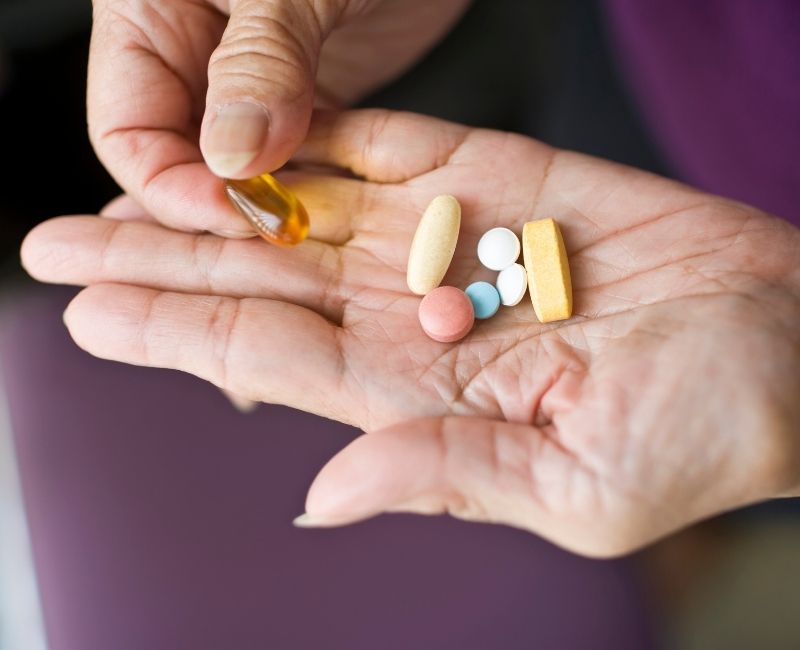 A close-up of a hand holding a variety of pills and supplements, including tablets and a softgel capsule, suggesting medication or treatment options.