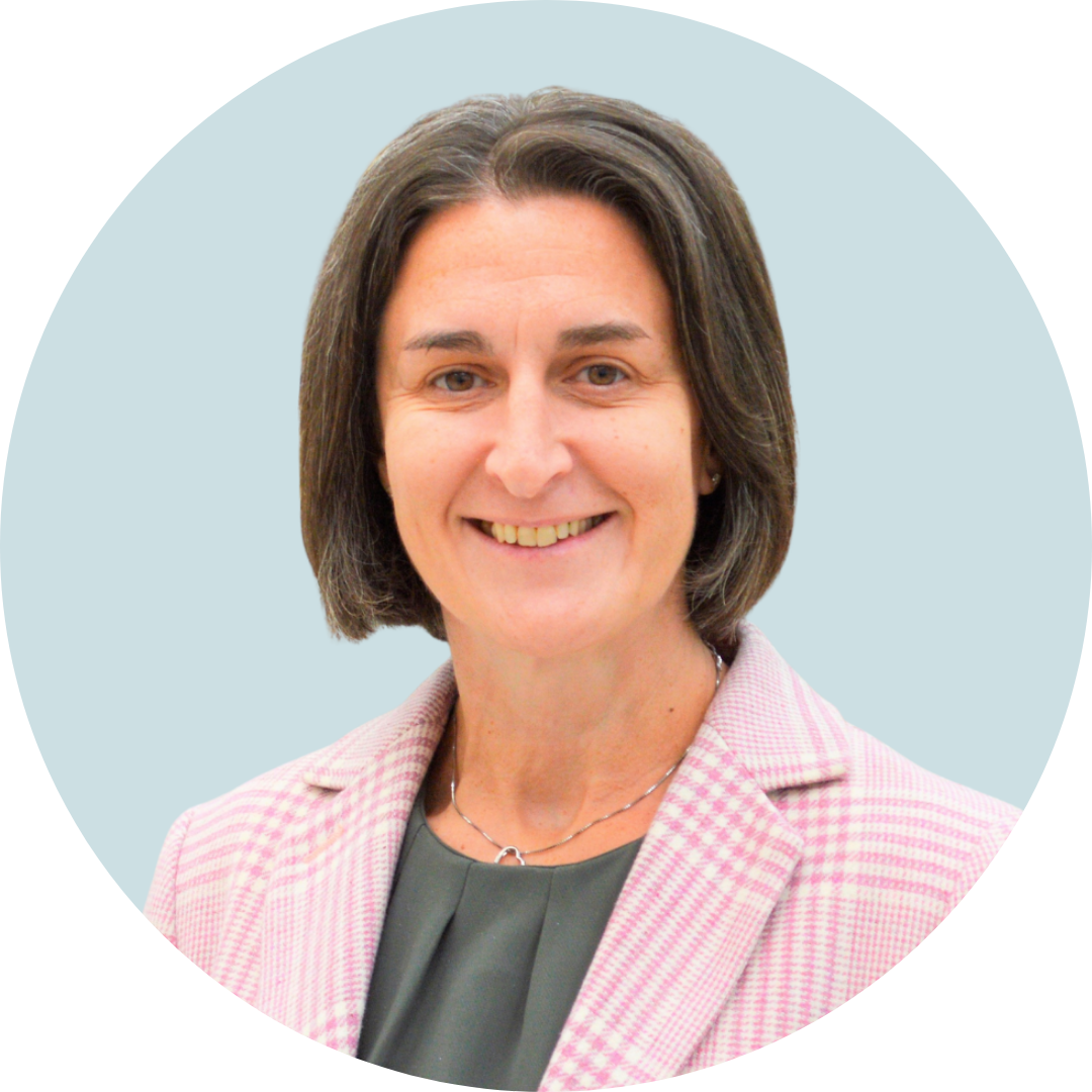 Professional portrait of a woman with short brown hair, wearing a pink check blazer and a green top, smiling directly at the camera