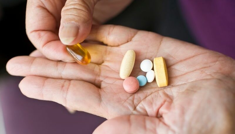 A close-up of a hand holding a variety of pills and supplements, including tablets and a softgel capsule, suggesting medication or treatment options.