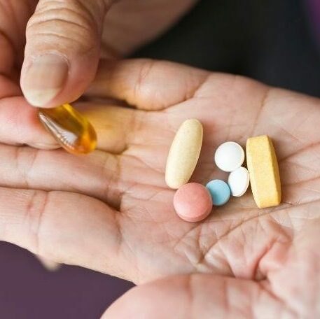 A close-up of a hand holding a variety of pills and supplements, including tablets and a softgel capsule, suggesting medication or treatment options.