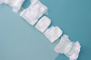 Several white incontinence pads arranged on a pastel blue background, suggesting personal care or incontinence management.